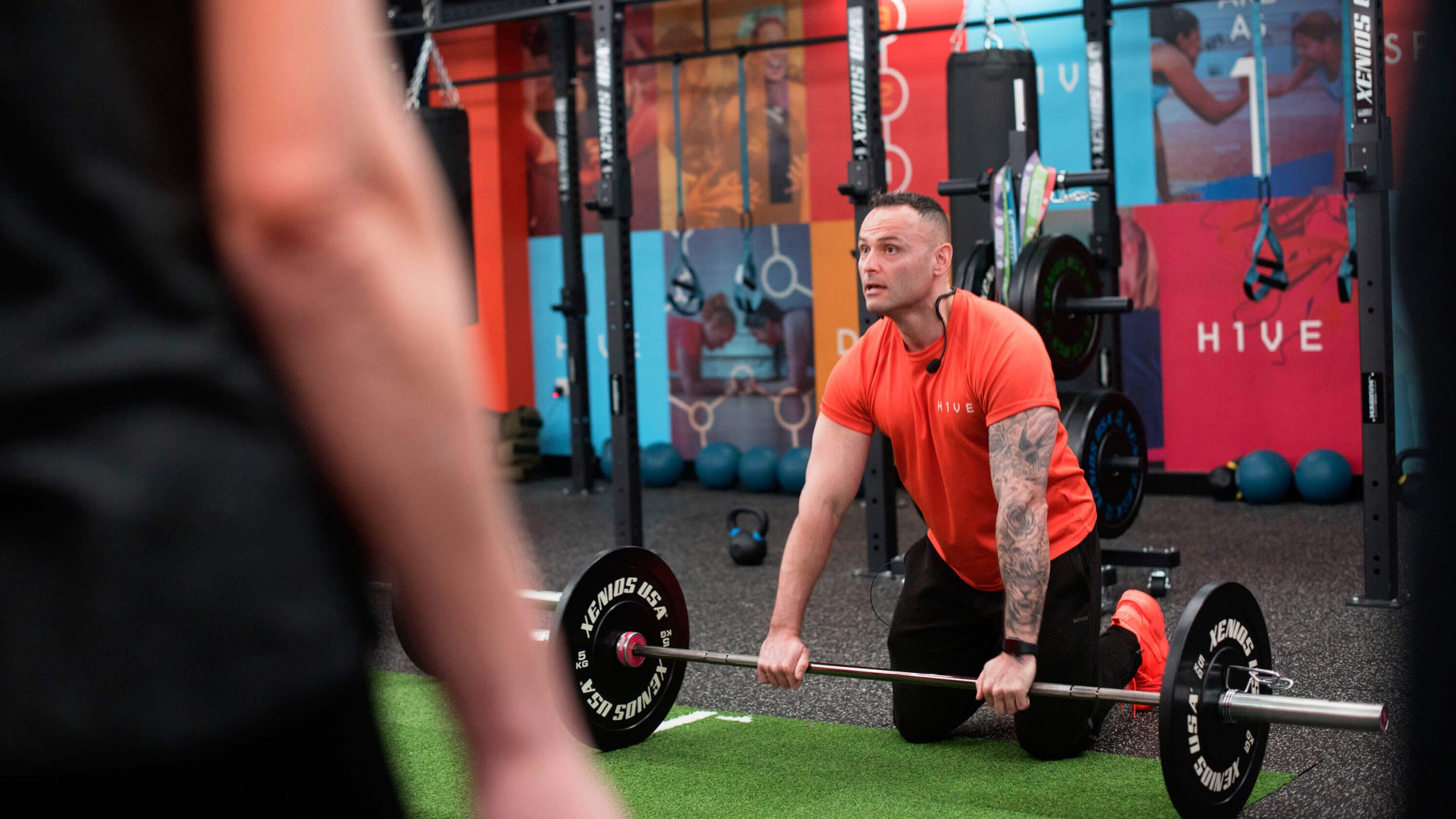 white muscular male instructor kneels down over a weight bar