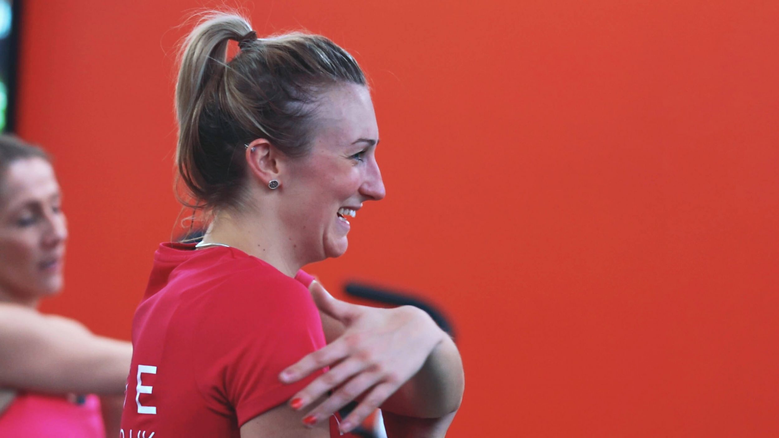 white woman in a red top is shown smiling turning to the side with a red background