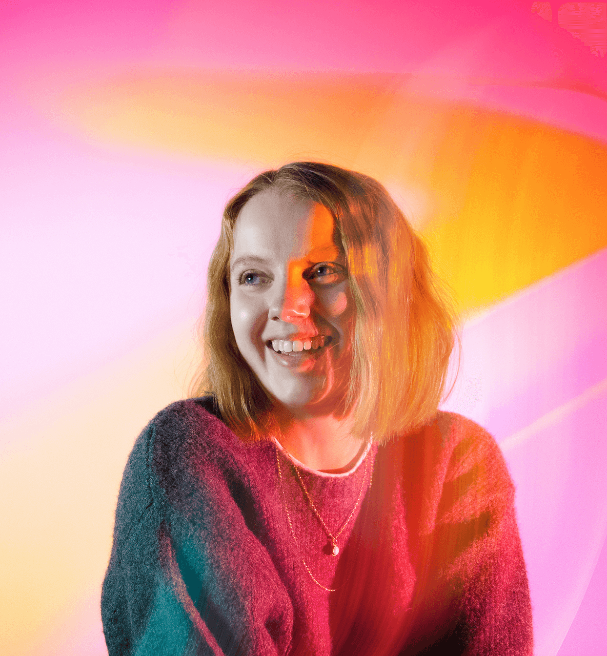 Alice, a blonde white woman in a baggy jumper is smiling looking to the side