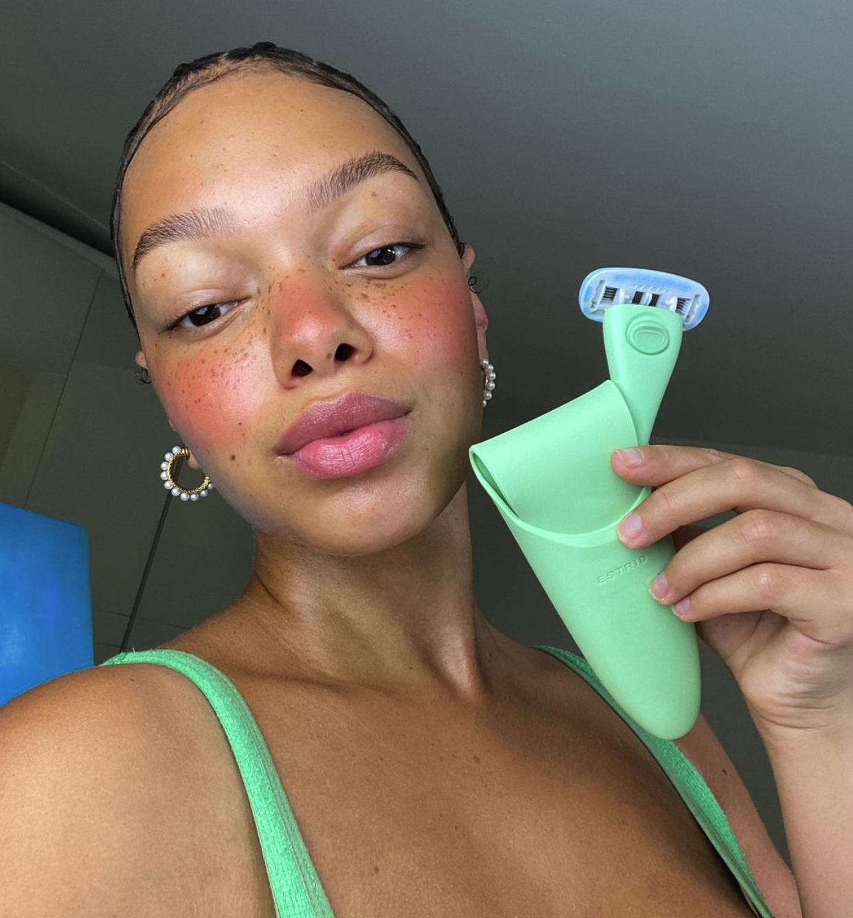 Pretty black woman with heavy blush in a green bikini top takes a selfie holding a matching Estrid green Razor and its matching holder,