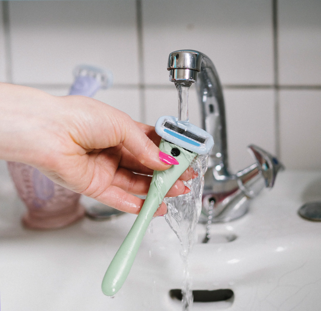Pastel green Estrid razor being run under a tap